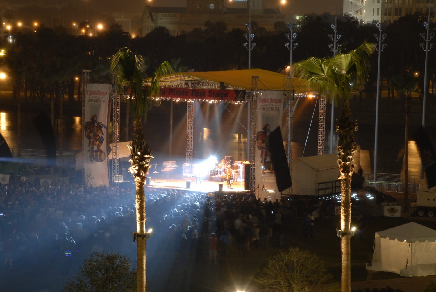 View of the MacDill Park stage at Gasparilla Pirate Fest 2025, surrounded by palm trees and a crowd illuminated by stage lights.