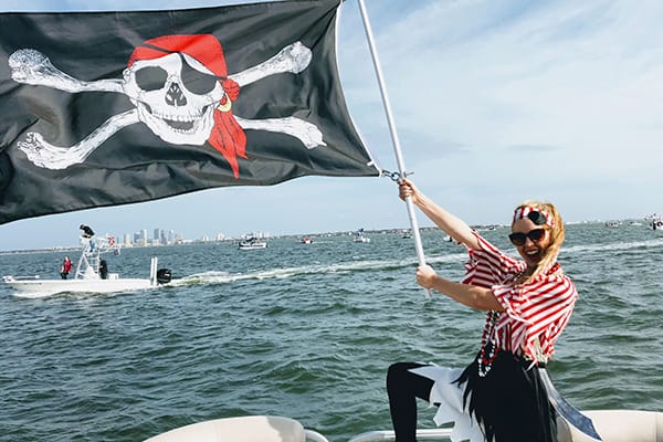 Smiling woman dressed as a pirate holding a Jolly Roger flag on a boat during the Gasparilla Invasion in Tampa Bay.