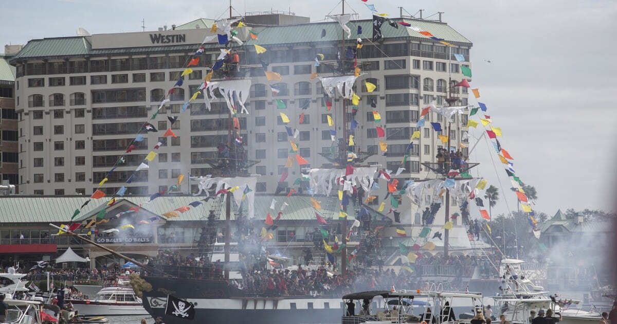 The Gasparilla pirate ship José Gaspar II sails in front of the Westin Tampa Waterside hotel, adorned with colorful flags during Gasparilla festivities.