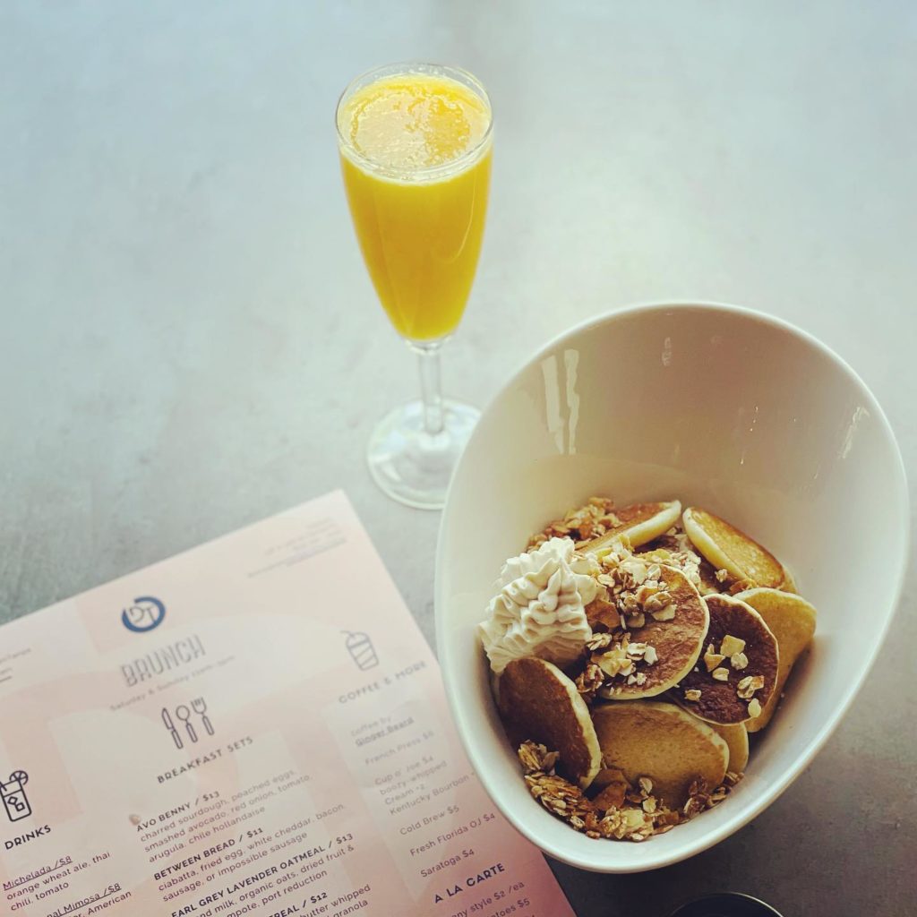 Image of a mimosa, an entree, and the menu during brunch at District Tavern