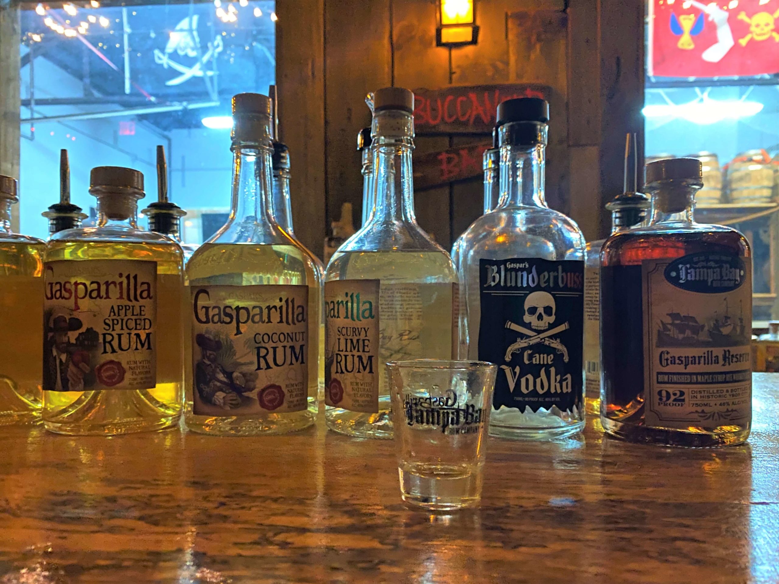 Rum Tasting at Tampa Bay Rum Company in Ybor City include multiple types of rum and one vodka. These bottles are set on a wood bar with a wood background