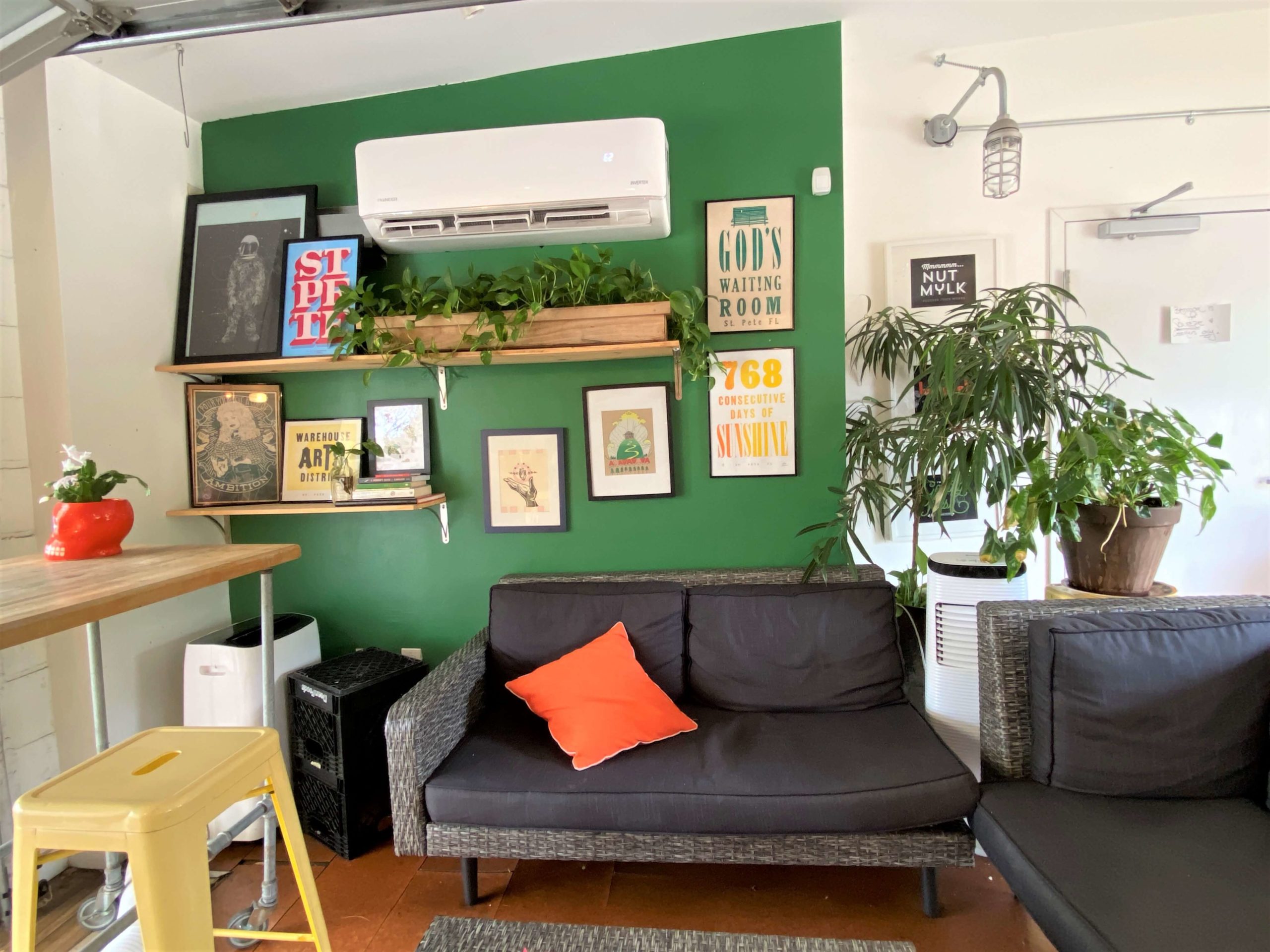 Squeeze Juice Company in St. Petersburg has a sitting area with a black couch, a green accent wall adorned with local Florida area, and plants around the entire sitting area. 