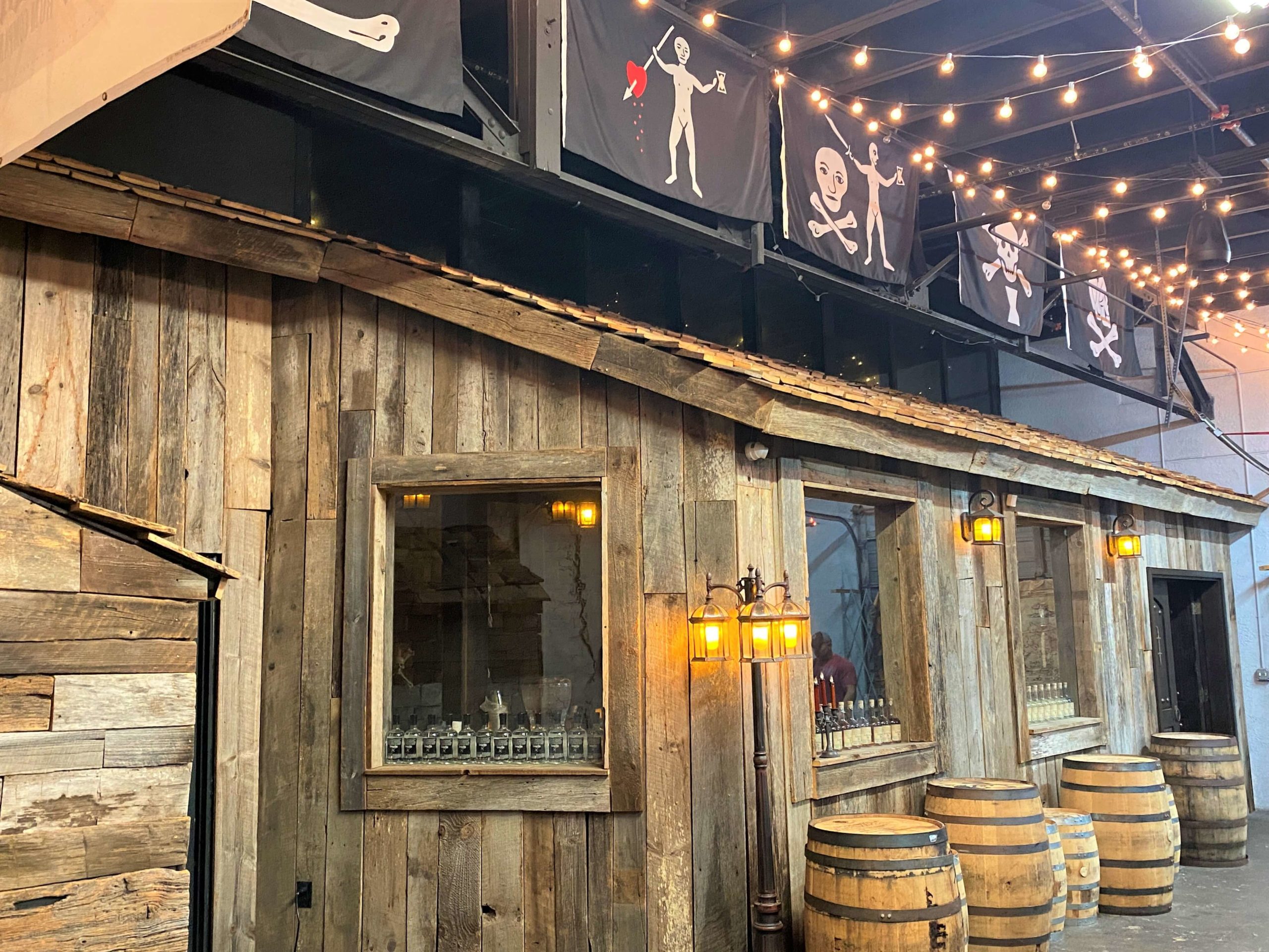 Tasting Room at Tampa Bay Rum Company in Ybor City is themed with pirate flags, weathered oak wood, lamps, and barrels.