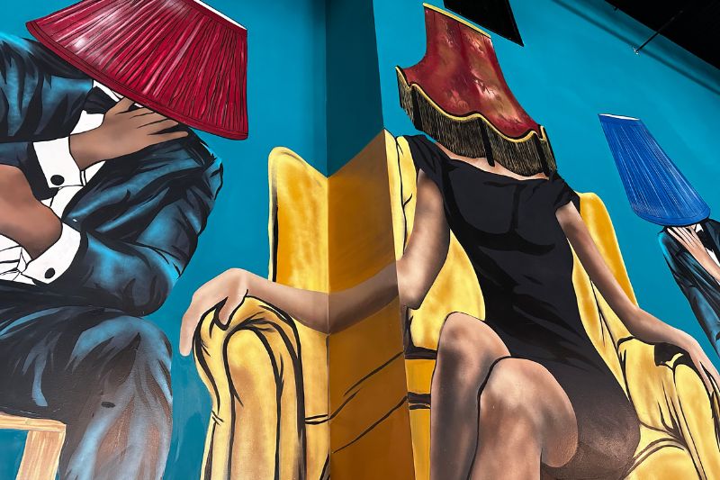 Mural of adults dressed in cocktail wear with lampshades on their heads at Lamp & Shade Craft Kitchen Orlando
