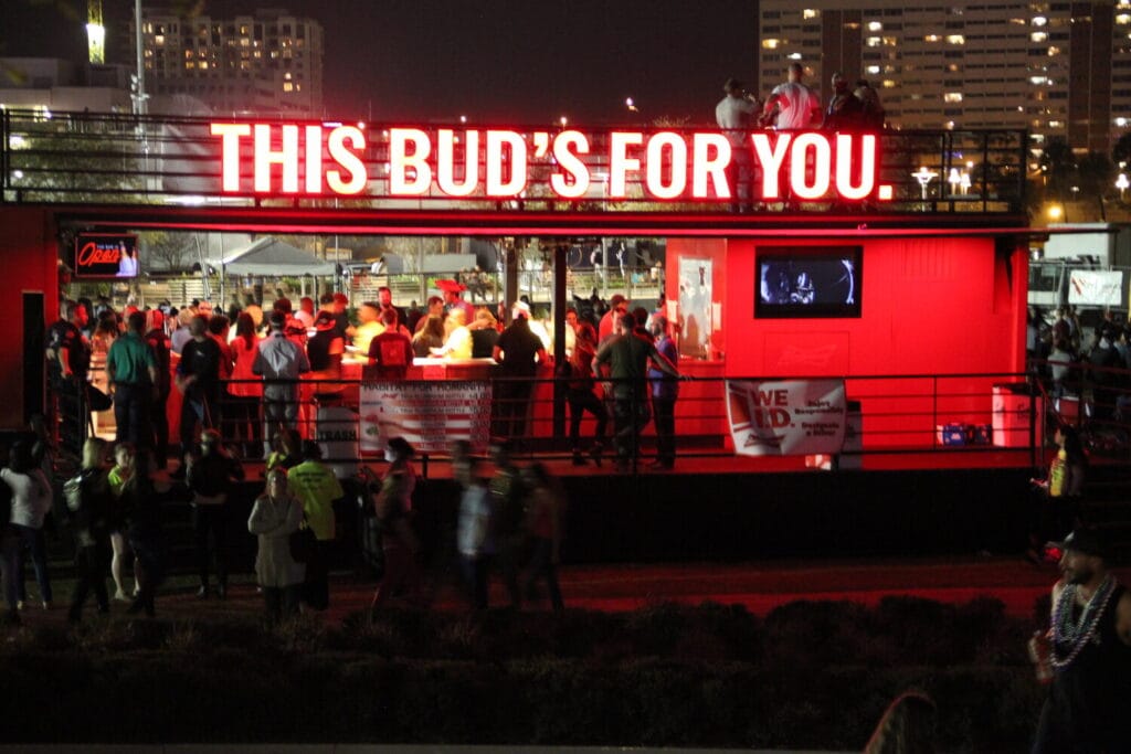 rowds gather at the illuminated Budweiser bar during Gasparilla Pirate Fest 2025 with a bright red sign reading, “This Bud’s for You.