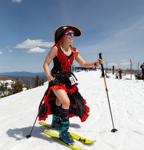 Smiling woman in a pirate costume skiing on a snowy mountain, demonstrating how to stay festive while braving the cold.