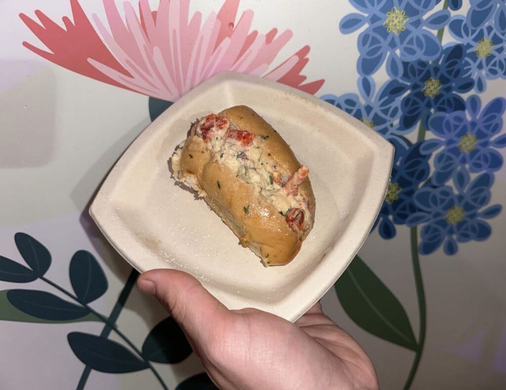 a mini lobster roll on a tan plate in front of a flowery white backdrop