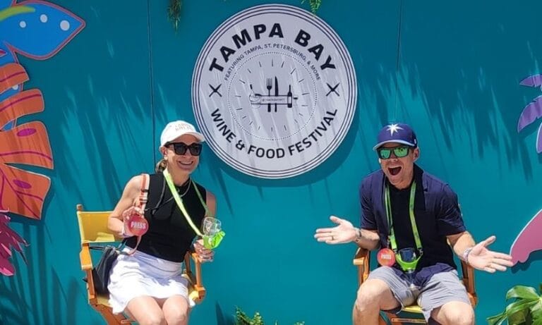 A couple sitting in chairs in front of teal backdrop with the Tampa Bay Wine & Food Festival logo