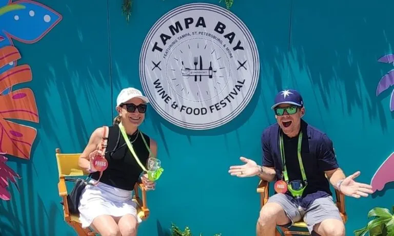 A couple sitting in chairs in front of teal backdrop with the Tampa Bay Wine & Food Festival logo