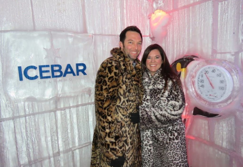 a couple in faux fur coats poses in front of ice sculptures at ICEBAR Orlando